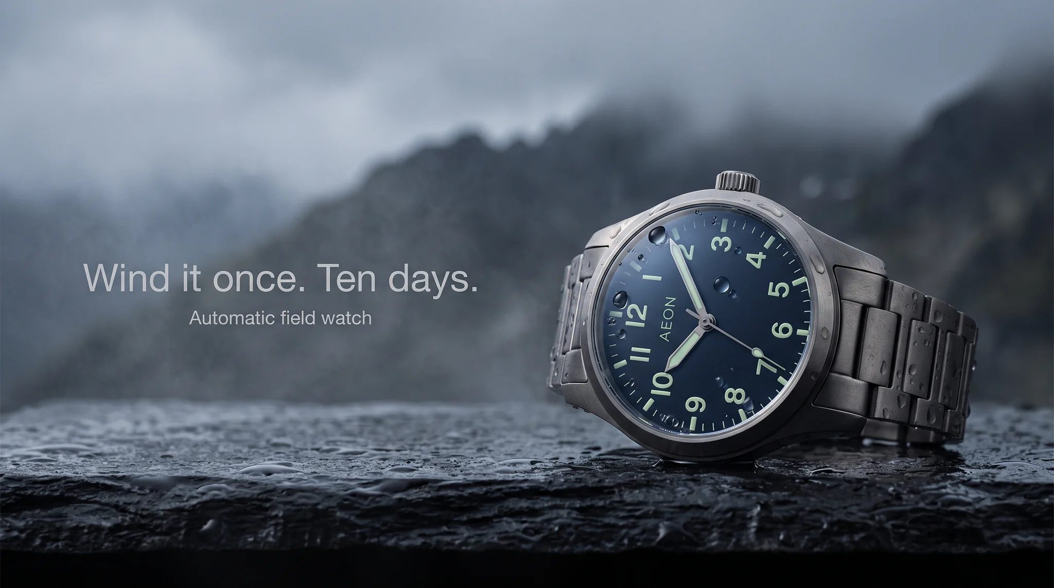 Example ad generated with Terrads: AEON titanium field watch on a rain-dark slate ledge before an alpine ridge, headline “Wind it once. Ten days.”